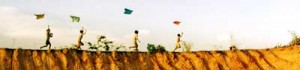 children flying kites on a winding green dyke during the summer months